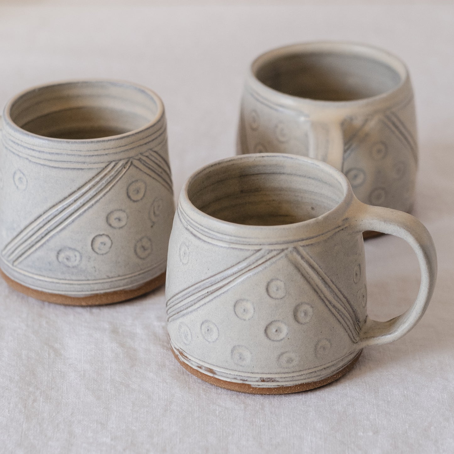 Three hand carved mugs with handles. Showing the design of lines and dots from all angles