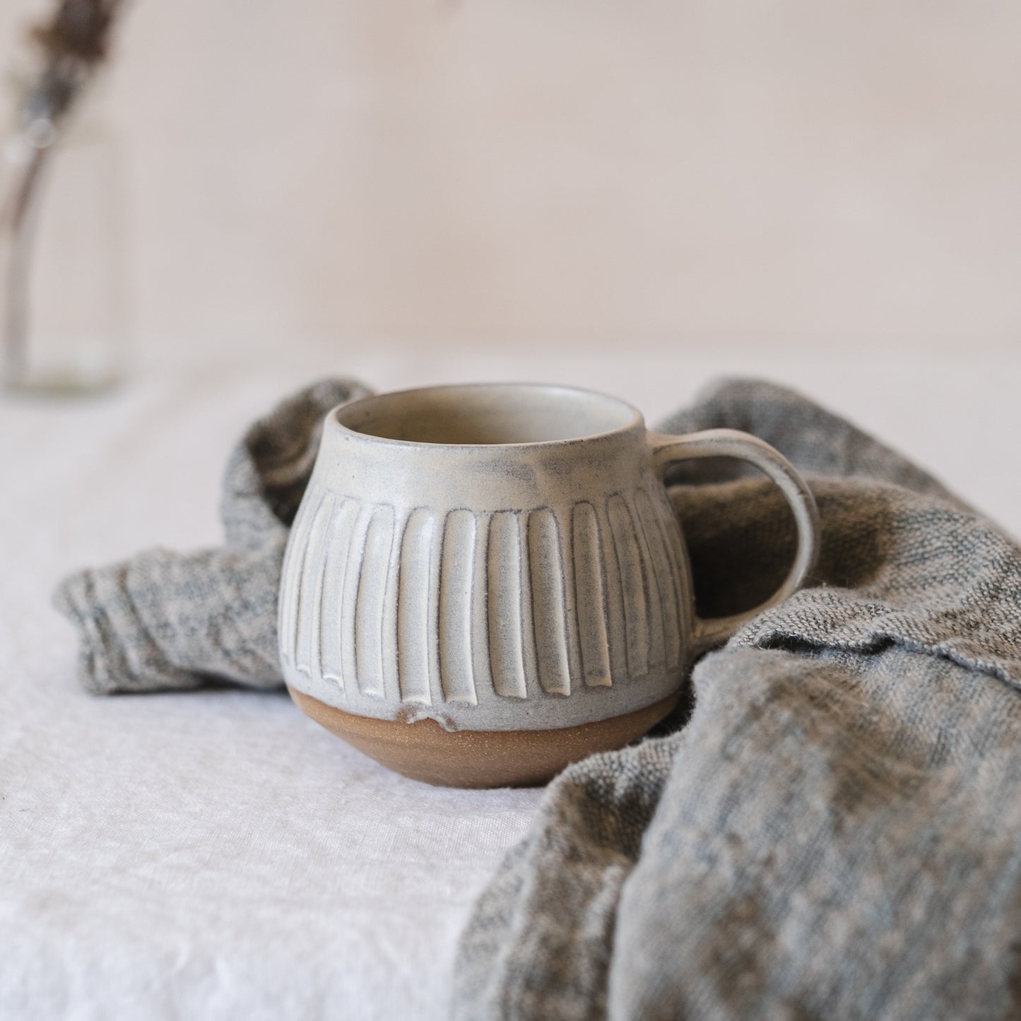 A large tea mug with line carvings in a soft yellow colour surrounded by an organic blue tea towel.