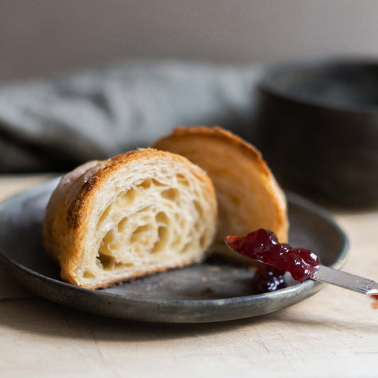 handmade ceramic breakfast set with granola bowl and side plate showing a buttery croissant and delicious strawberry jam.