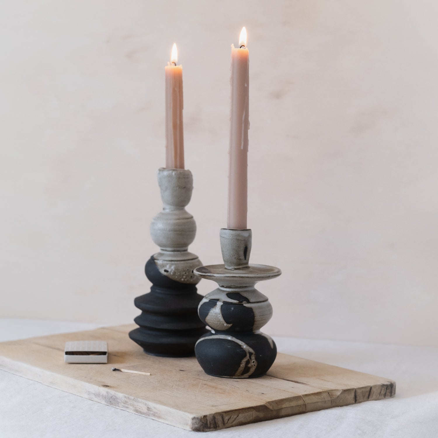 Two handmade black and white ceramic candlesticks in different sizes with pink tapered candles. A box of matches sits to the left of the unique candle holders