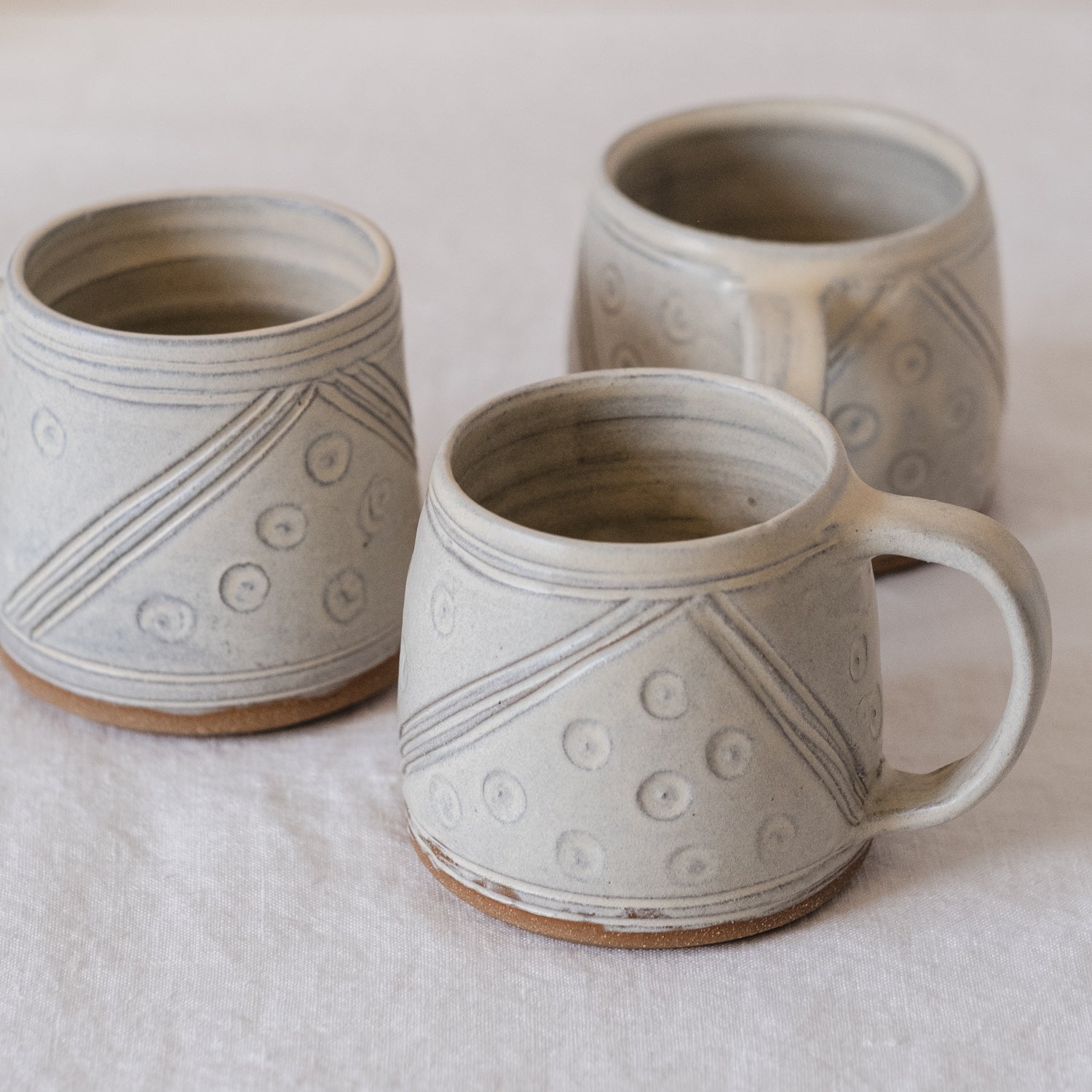 Three hand carved mugs with handles. Showing the design of lines and dots from all angles