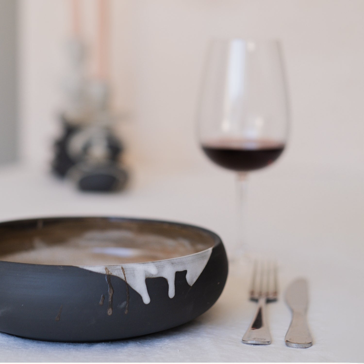 Deep Ceramic Pasta Bowl With Golden Interior and a white drip technique displayed on the outer edge of the bowl. A dinner setting with a wine glass and cutlery on a white linen tablecloth