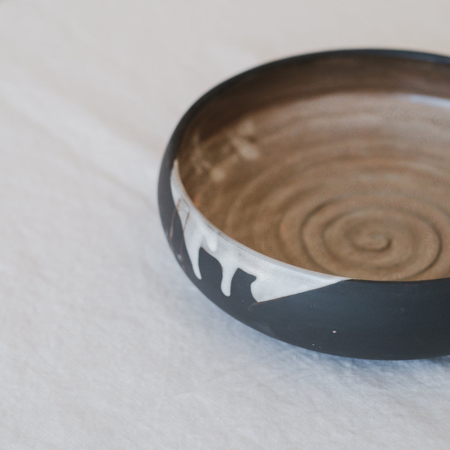 Handmade ceramic pasta dish or serving bowl with a golden colour glaze on the inside and a dark earthy colour on the outside with a white drip glaze.