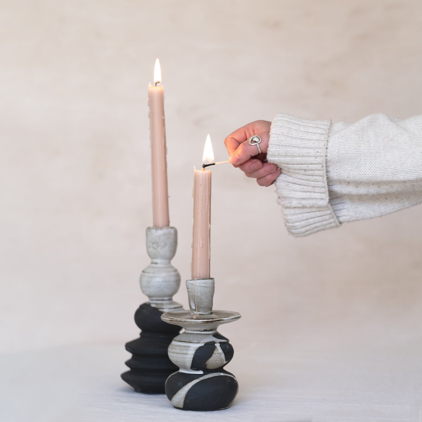 Ceramic Candlesticks beautifully handmade embracing the wabi sabi style. A hand reaches in to light the tapered candle on the right